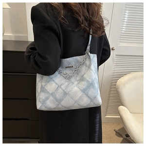 Detail of light blue quilted denim tote bag with silver metal chain and logo decoration