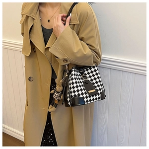 Detail of checkered bucket bag with leather strap and cute rabbit charm on a model