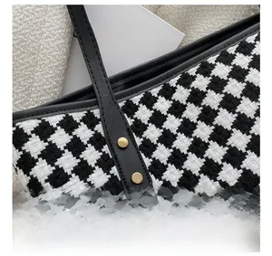 Close-up of houndstooth tote bag detail featuring black leather handle and gold metal rivets