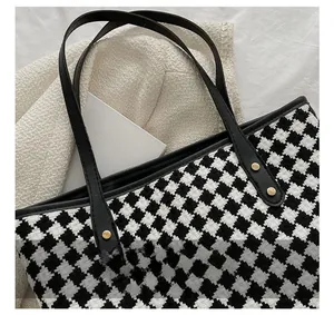 Detail of houndstooth tote bag featuring leather straps and golden rivet accents