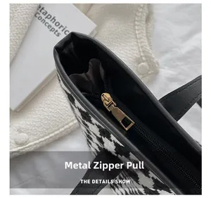 Close-up of golden metal zipper hardware on a black and white houndstooth tote bag
