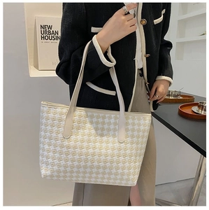 Close-up of textured tweed tote bag in beige with reinforced leather handles on a model