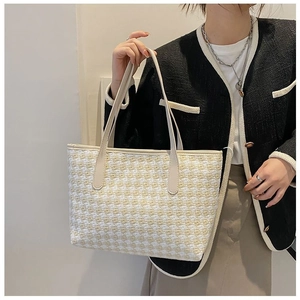 Detail of yellow and white woven tote bag with smooth beige faux leather straps