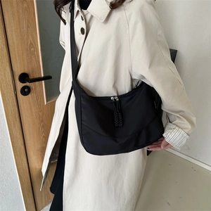 Detailed view of black nylon crescent bag with woven zipper pull worn over shoulder