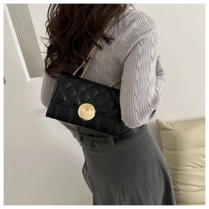 Détail du sac bandoulière matelassé noir avec fermoir rond doré et bandoulière chaîne