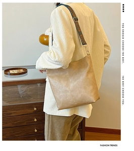 Close-up of khaki bucket bag with Bohemian embroidered wide strap on model in indoor setting