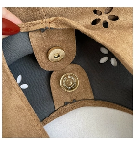 Close-up of brown suede tote bag with hollow floral pattern and magnetic snap buckle