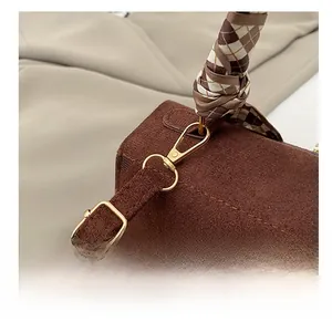Close-up of brown suede Kelly bag featuring gold metal hooks and a plaid scarf handle