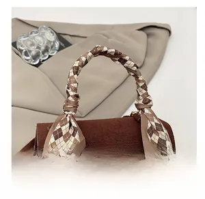 Close-up of brown corduroy handbag featuring a silk scarf handle and metal buckle lock
