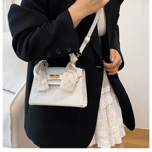 Detail of white leather trapezoid bag with silk scarf handle and metal lock detail