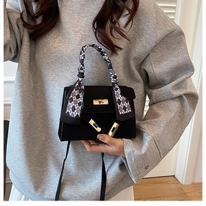 Close-up of black matte trapezoid bag with gold lock and decorative silk scarf on handle