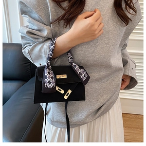 Detail of black leather Kelly handbag with gold lock and checkered scarf on handle