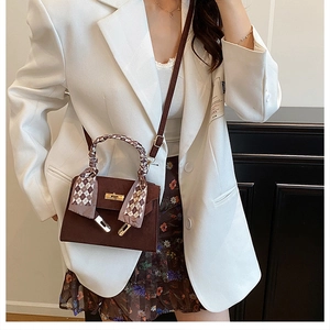 Detail of dark brown leather handbag featuring a gold buckle and silk scarf on handle