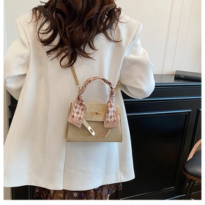 Detail of beige structured handbag featuring a scarf-wrapped handle on a white blazer