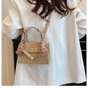 Detail of a beige PU leather handbag featuring a silk scarf wrapped handle and gold lock