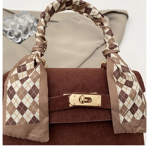 Detail of dark brown corduroy handbag featuring a silk scarf wrapped handle and gold lock