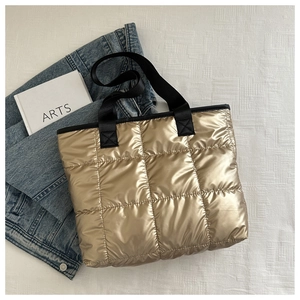 Flat lay of metallic gold quilted tote bag with black handles and lifestyle accessories