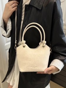Elegant cream white handbag with metallic rings and top handle shown on a model