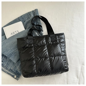 Detail of black quilted tote bag with polished finish and sturdy nylon straps on fabric