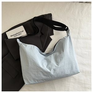Close-up of light blue crescent pillow bag with adjustable wide black strap on fabric