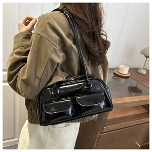 Close-up of black patent leather shoulder bag with two front pockets on a model