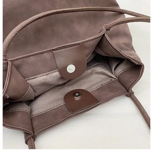 Macro detail of dark brown matte leather tote with silver magnetic snap and neat stitching