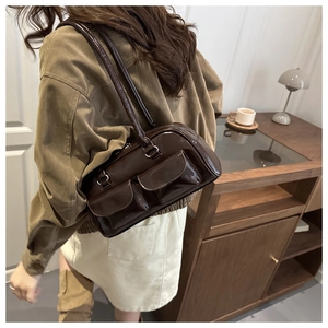 Deep brown glossy shoulder bag with functional pockets shown in a cozy interior setting