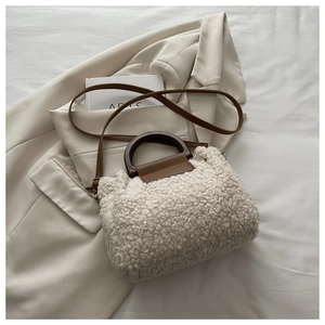 Détail d'un sac cabas en fausse fourrure crème avec anses marron sur un blazer élégant