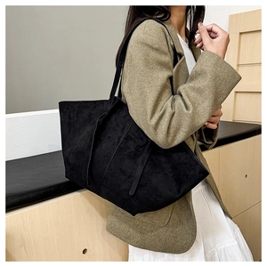 Detail of a large black matte leather tote bag worn by a model in casual office style
