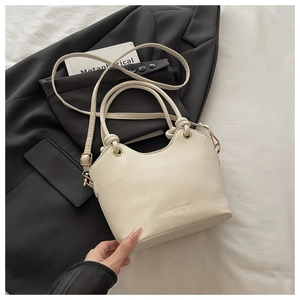 Detail view of white bucket bag with gold hardware and brand lettering on black blazer
