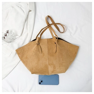 Flat lay of large taupe suede tote bag with slim handles and knot detail on white fabric