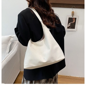 Side view of a large white faux leather hobo shoulder bag worn by a model in a minimalist room