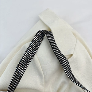Detail of white woven fabric with black sequined decorative band and silver accents