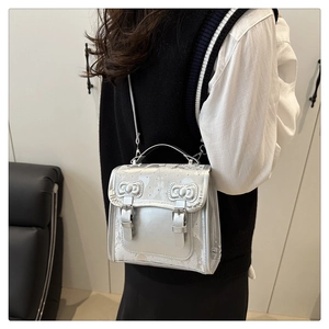 Detail of silver metallic crossbody bag featuring bow accent and double buckle design
