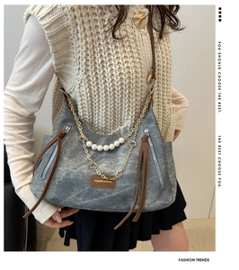 Detail of grey denim tote bag featuring pearl chain accents and premium leather zipper pull