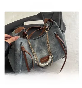 Detail of grey-blue washed denim shoulder bag with pearl chain and brown leather accents