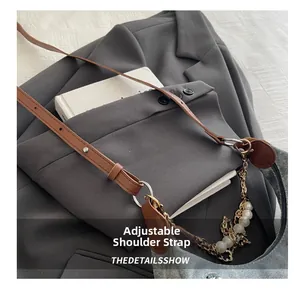Detail of adjustable leather strap and decorative pearl chain on gray denim handbag