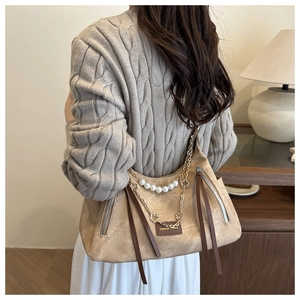 Detail view of beige shoulder bag featuring pearl chain, flower pendant, and long tassels