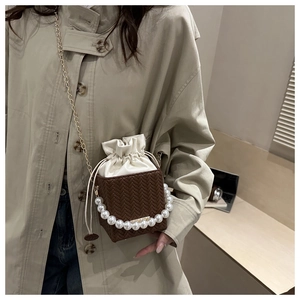 Detailed view of woven bucket bag with pearl handle and golden chain on beige trench coat