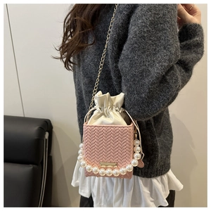Pink woven bucket bag featuring pearl beaded handle and golden chain detail on a model