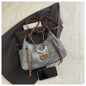 Detail view of grey washed denim handbag featuring pearl chain and leather straps
