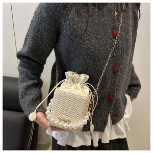 Detail of cream woven square bag featuring large pearl handle and gold chain strap