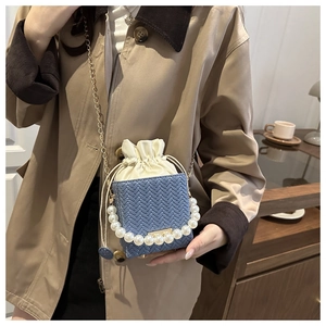 Detail showing woven bucket bag with elegant pearl handle and fine gold chain strap