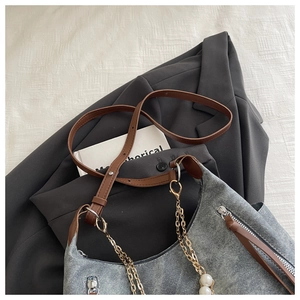 Detail of grey denim handbag with pearl chain and brown leather strap on blazer