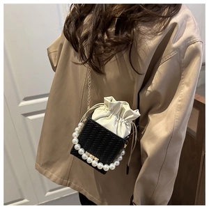 Detail of woven bucket bag featuring pearl handle and gold chain strap on a model