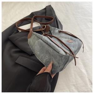 Detail of grey washed denim hobo bag with brown leather strap and silver zipper on suit