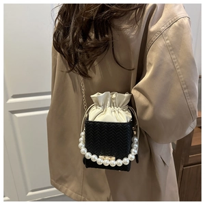 Close-up of woven bucket bag with pearl handle and chain strap worn by a model