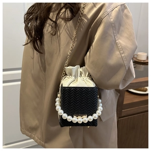 Detail of black woven bucket bag featuring large pearl handle and gold chain strap