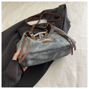 Detail of grey washed denim hobo bag with fringe zipper, pearl chain, and leather strap