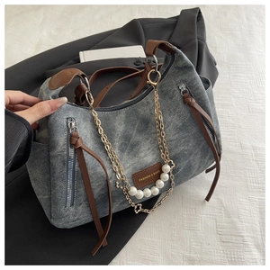 Detail of vintage gray denim handbag featuring pearl chain charm and brown leather trim
